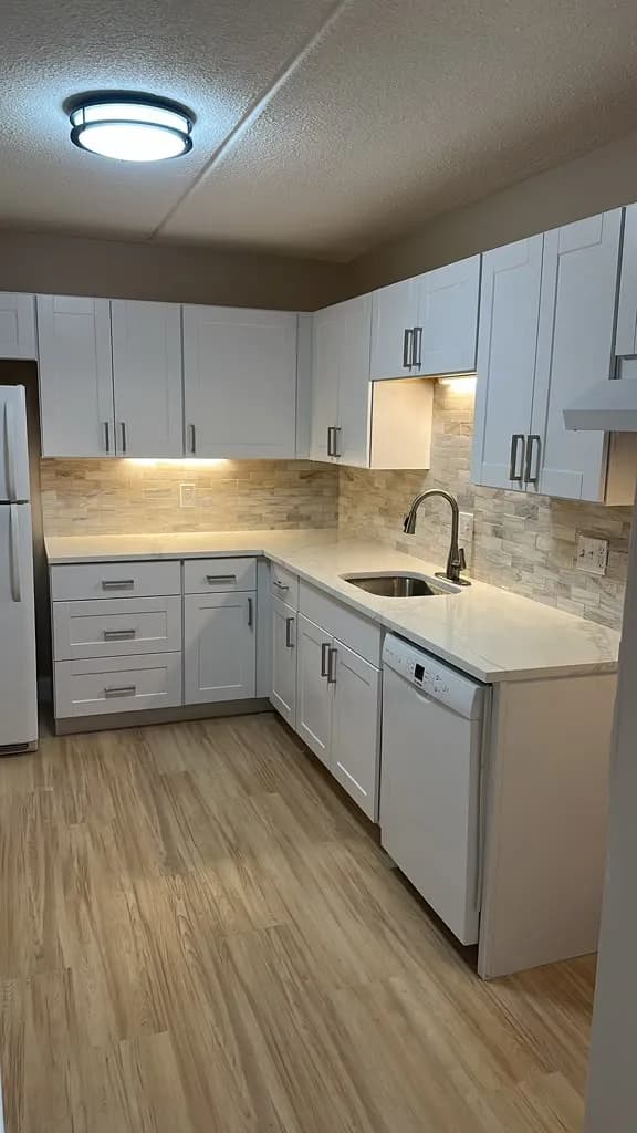 Remodeled kitchen with white cabinets, quartz counters, and stacked stone backsplash