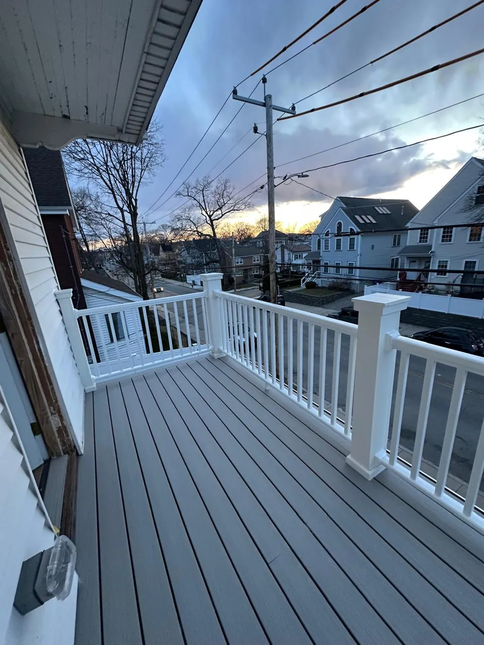 Second-floor porch with composite decking and vinyl railings at sunset