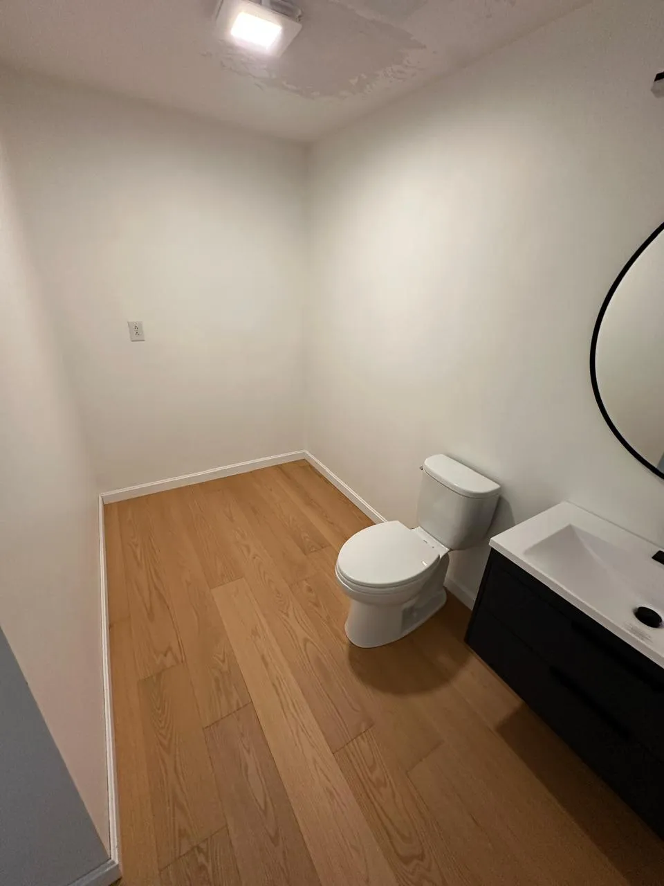 Powder room with hardwood floor, floating vanity, and round mirror